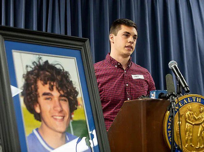 Person standing near a photo of boy speaking in a conference.