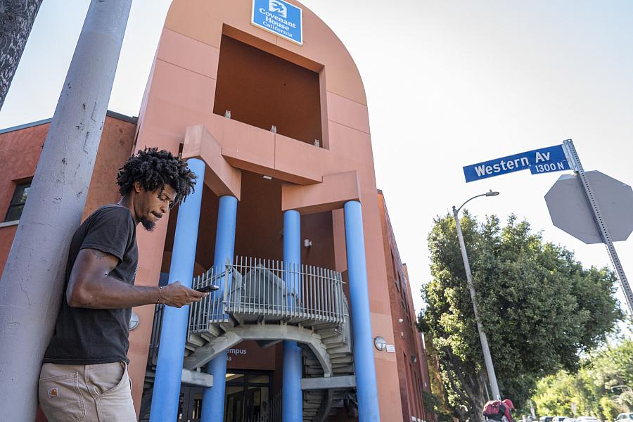 Person standing in front of a orange-blue building against a pole