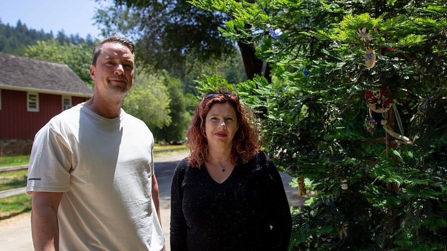 Two people next to each other one wearing a white top and another wearing a black top and greenery in the background