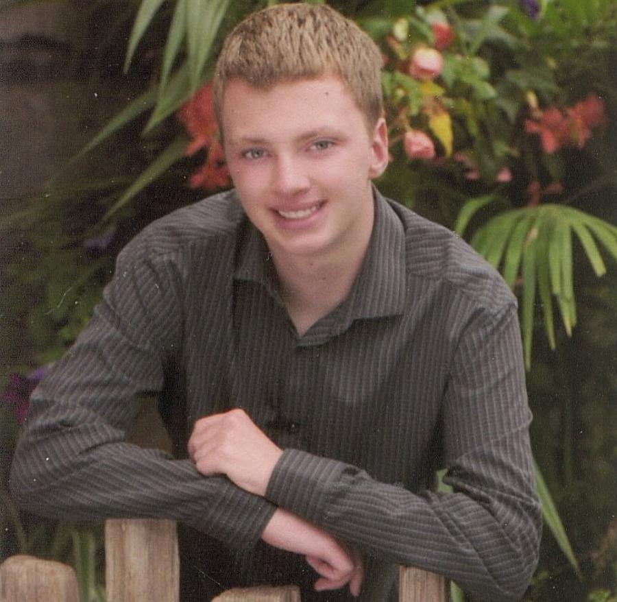 Person with brownish shirt, golden hair sitting on a chair against a tree
