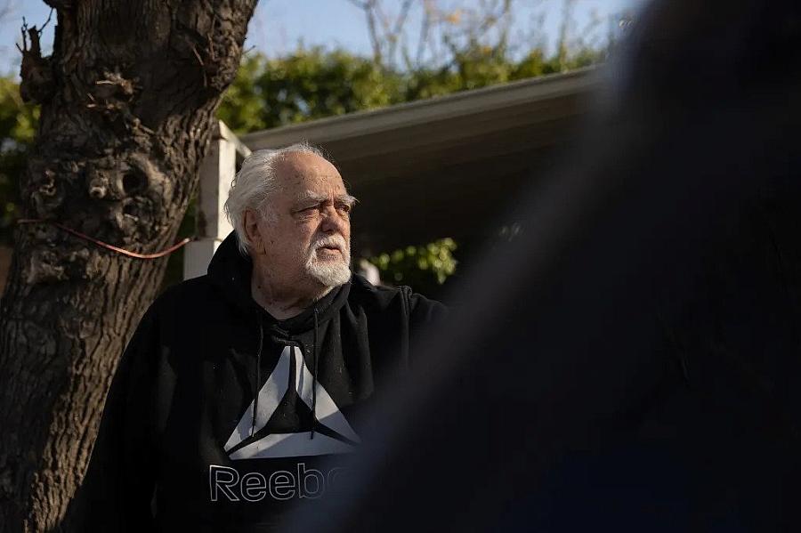 An 87 year old man standing near a tree.