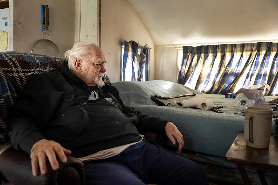 An old man sitting on couch in his home near bed