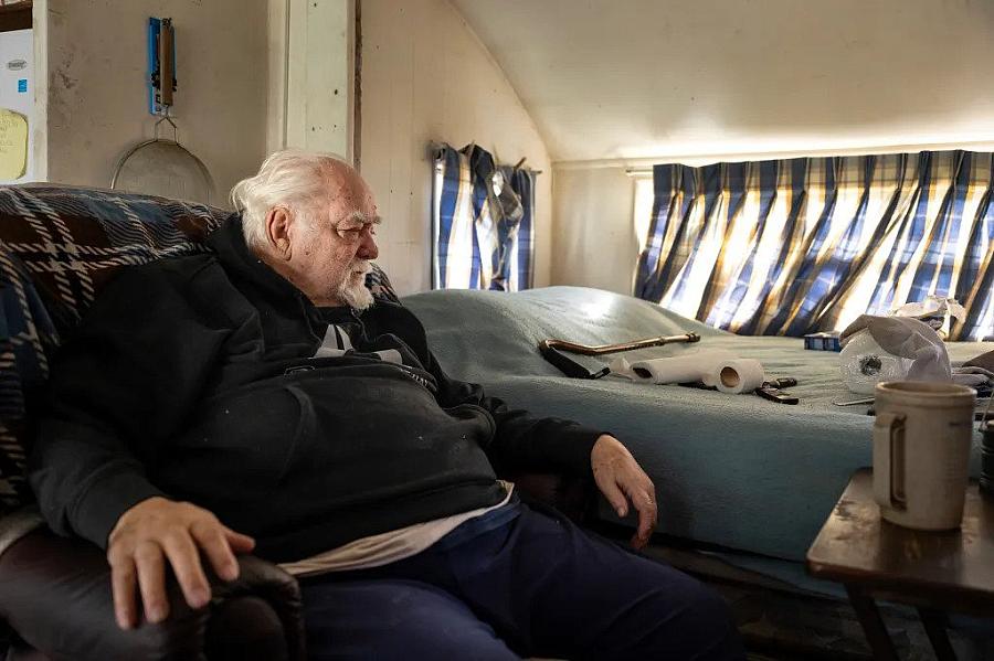 A man sitting on the couch besides his bed.