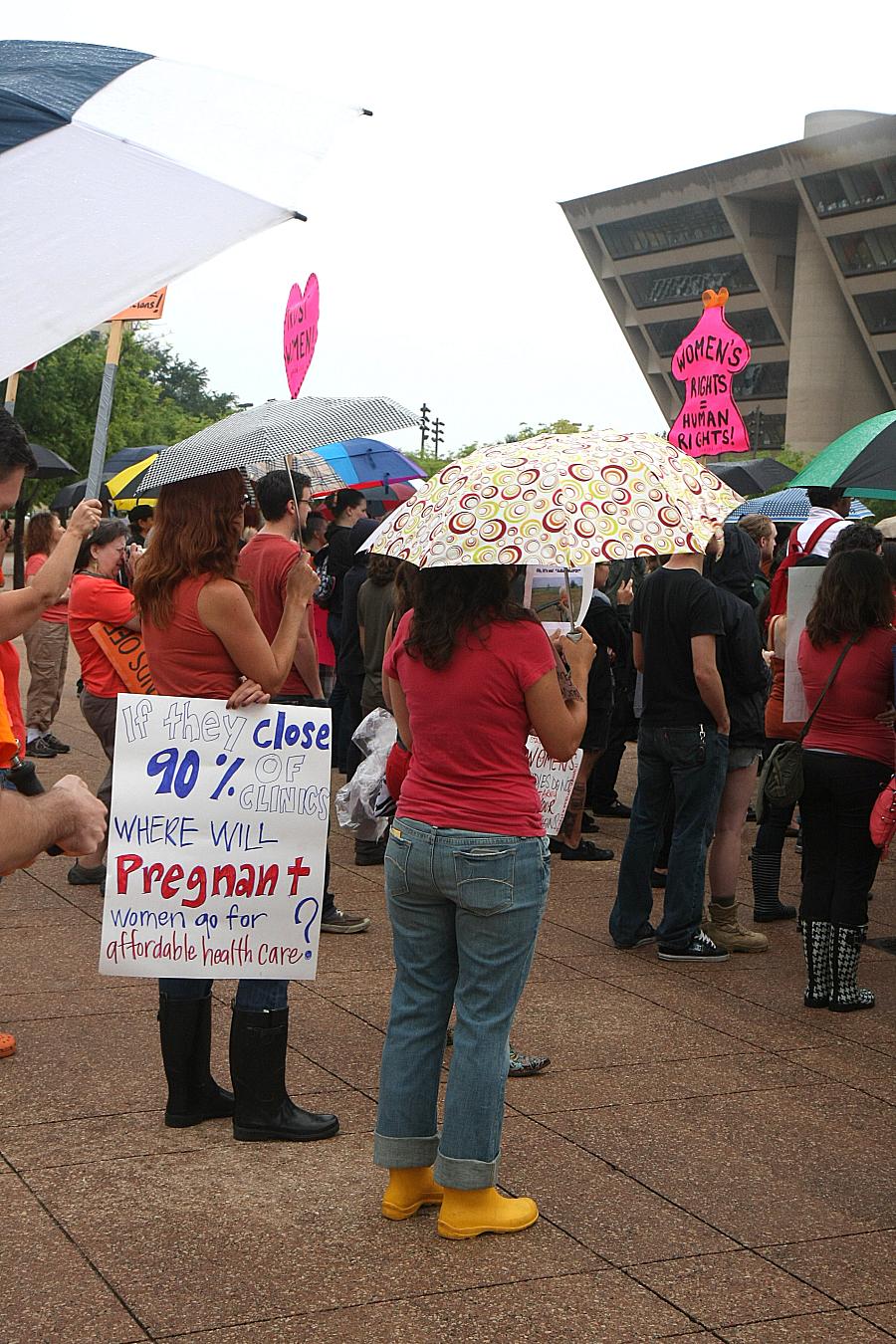 People in protest with a person holding banner saying "If they close 90% clinics where will pregnant women go for affordable health care"