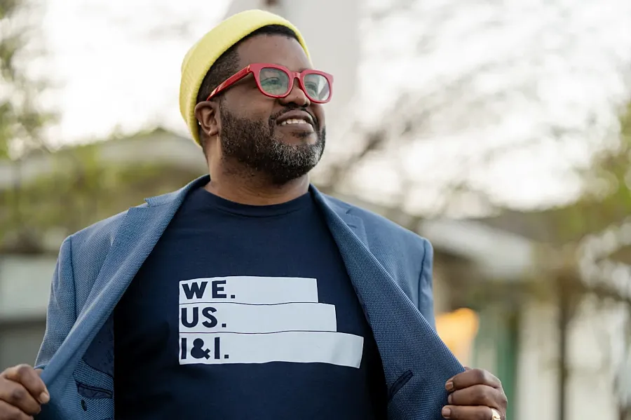 Person in blue coat with dark blue t-shirt, red spectacles and yellow cap