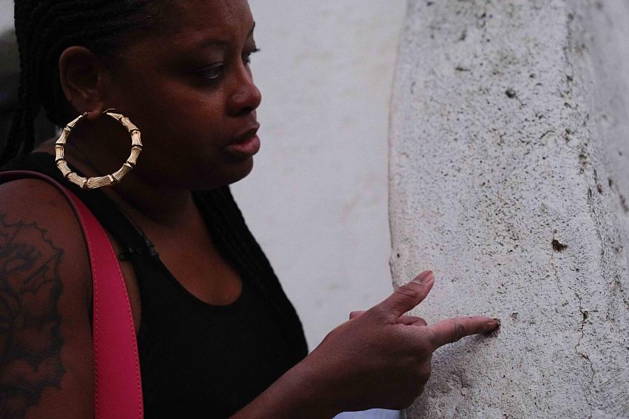 Image of a person pointing at the wall with bullet holes