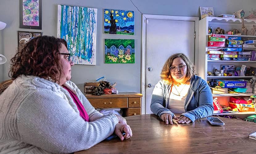 Two women sitting at a wooden table in a room filled with colorful paintings and board games.