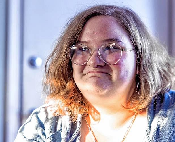Close-up of a young woman with glasses, looking slightly to the side in natural indoor light.