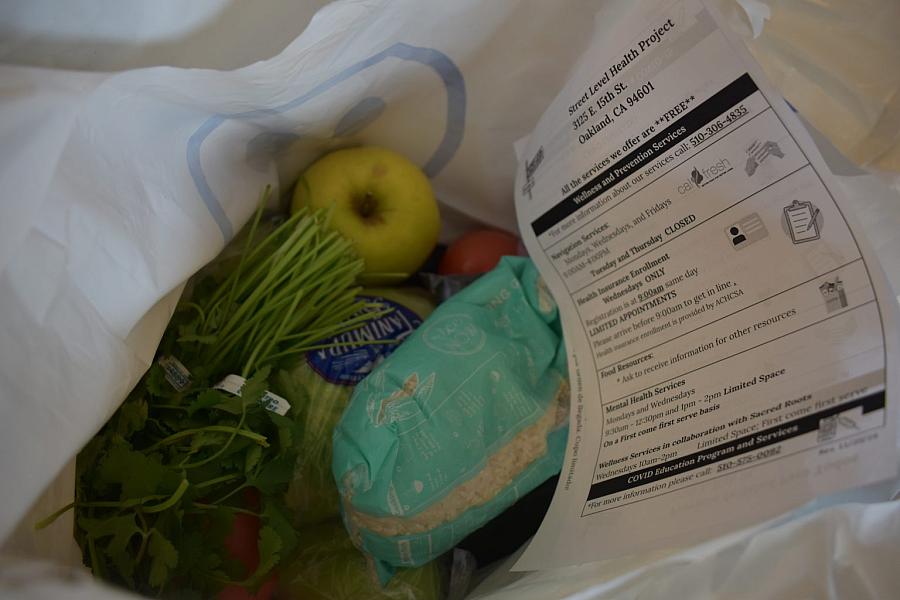 A close-up of a bag containing rice, cilantro, apple, and a flyer with community service info.