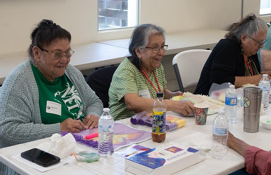 Three native women do crafts and share a laugh together at a table