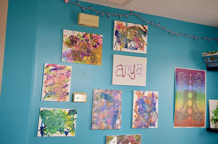 Children’s colorful artwork and the name “Arya” are displayed on a bright blue wall, with a chakra poster and games on nearby shelves.