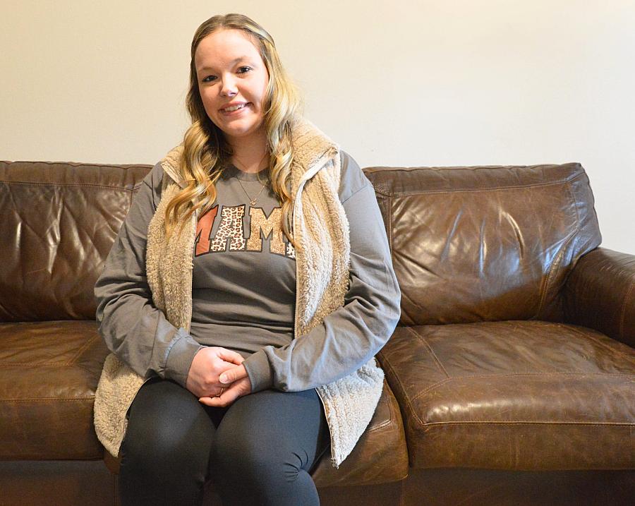 A woman sits on a brown leather couch and smiling