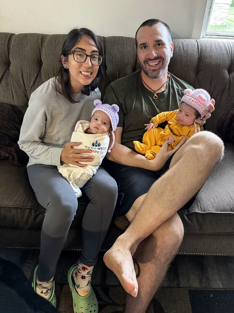 2 people seated on a couch holding babies