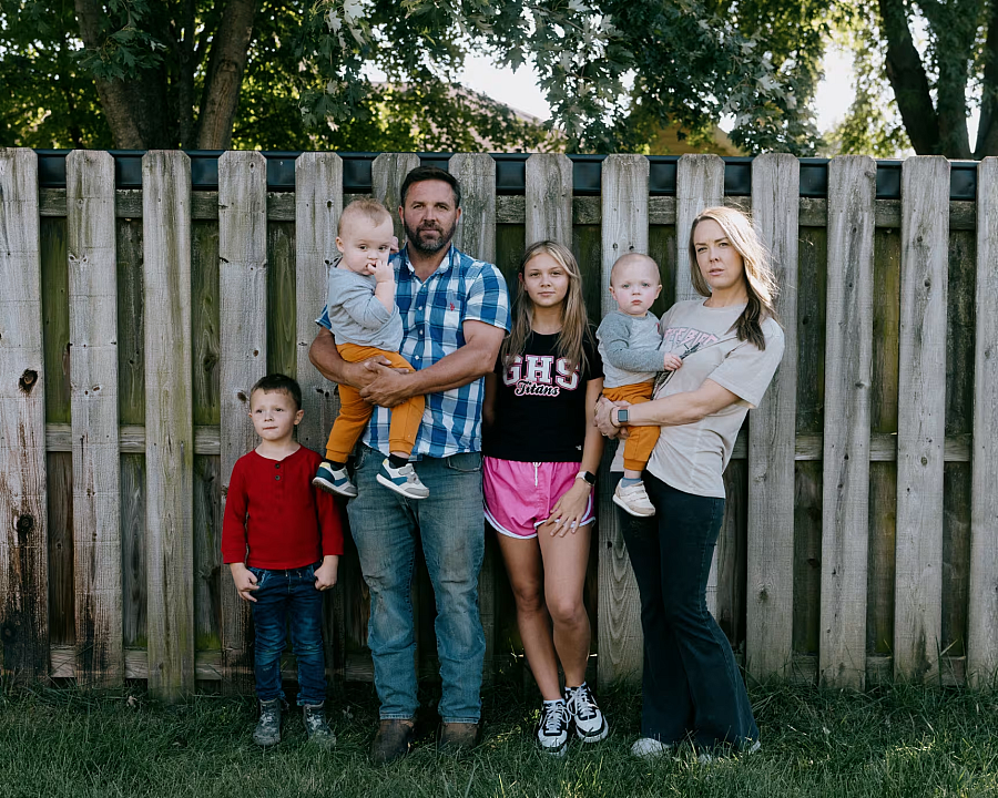 2 people standing with 4 children in front of a fence 