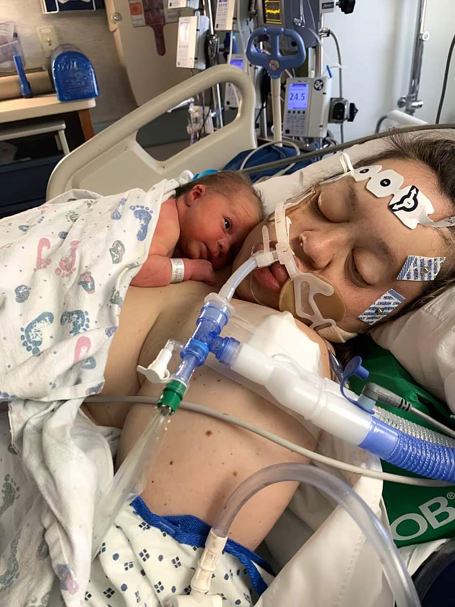 Person in a hospital bed with medical equipment surrounding them and a baby on their chest