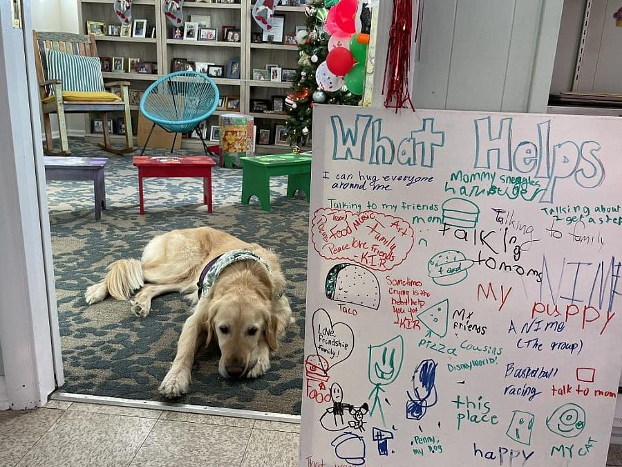 Therapy dog lies near a decorated board listing what helps children cope with loss.