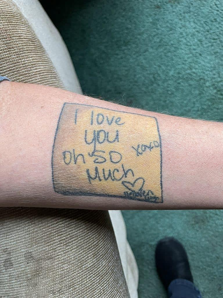 Close-up of a forearm tattoo showing a handwritten note that says, “I love you oh so much” with a heart and “xoxo.”