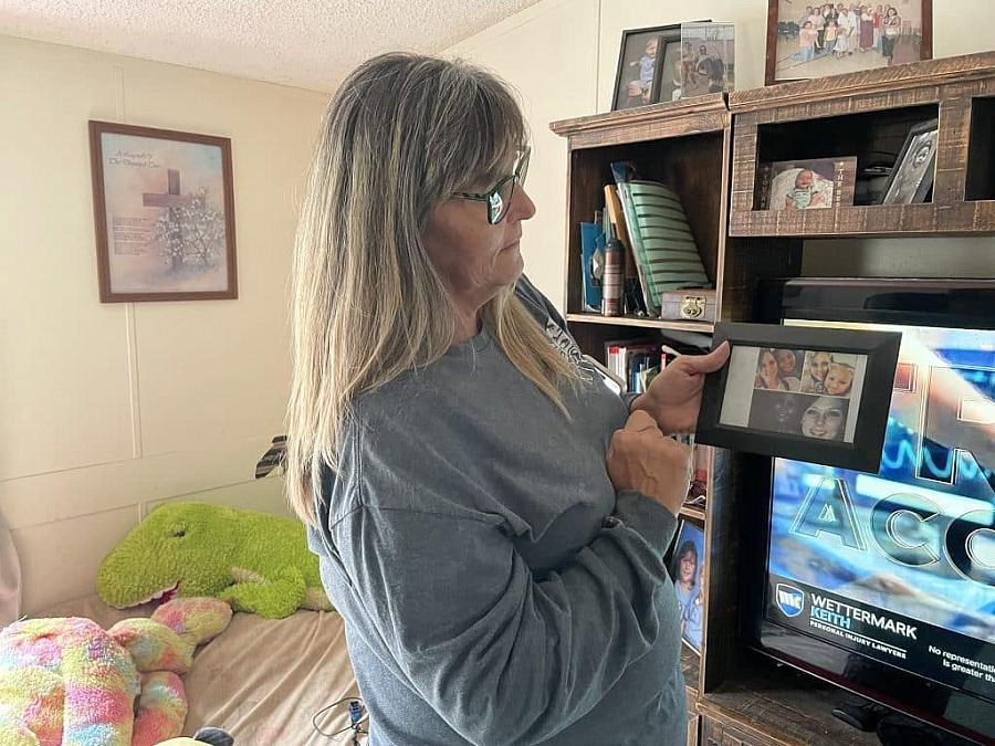 Woman shows a framed photo collage of her daughter inside a cozy living room.