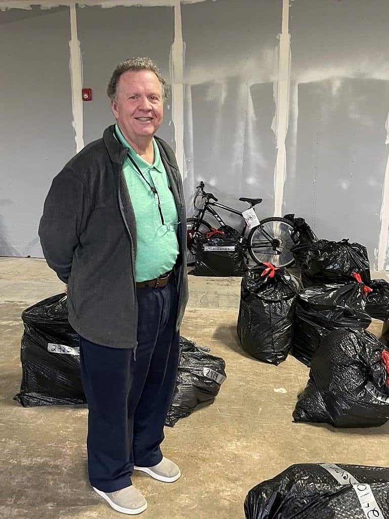 Man stands in a storage room surrounded by black bags filled with donated gifts.