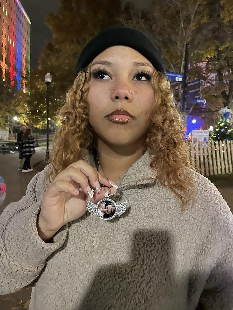 Young woman holds a memorial necklace with a photo of a loved one at night.