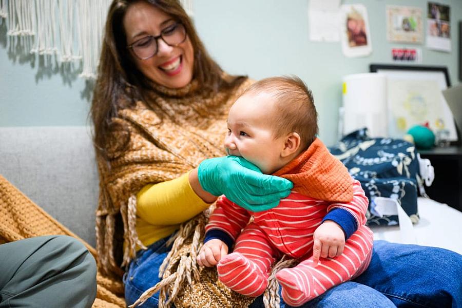 Person holding an infant and infant biting persons hand which has a glove on it