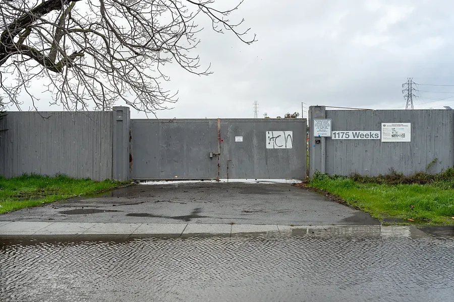 Gray gate at 1175 Weeks with warning signs and puddles in front.