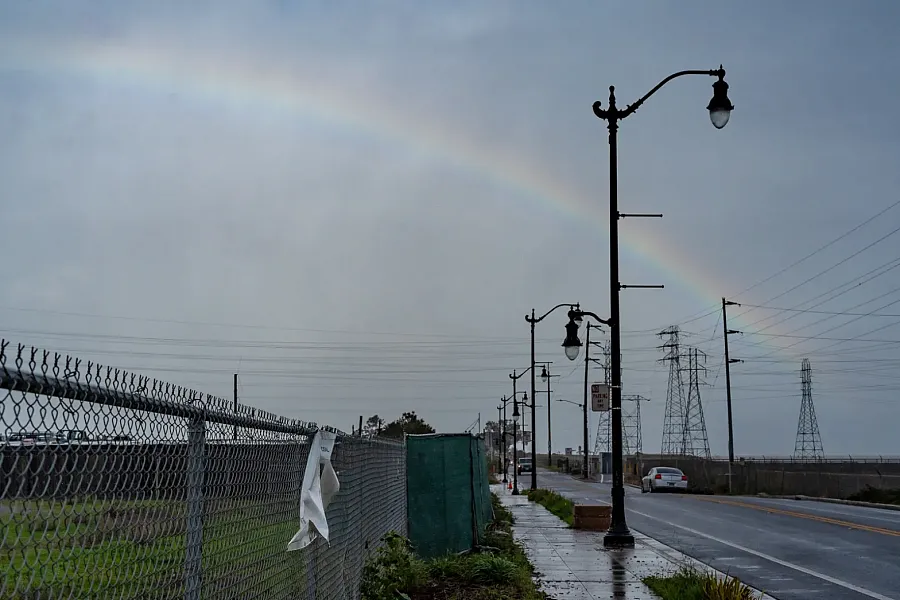 Street view with chain-link fence, rainbow, and utility poles.