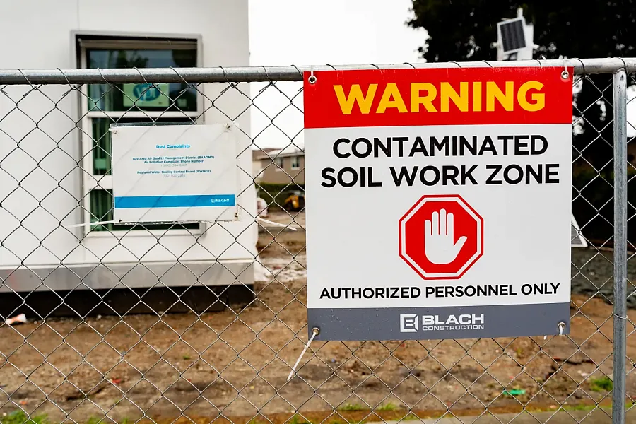 Contaminated soil warning sign on a chain-link fence.