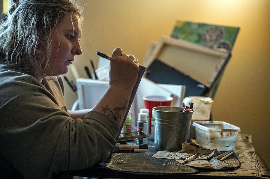 Woman painting on canvas in hand with colors on table in front of her.