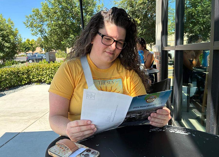 Woman reading water quality report — A woman in glasses and a yellow shirt sits outside reading a city water quality report.