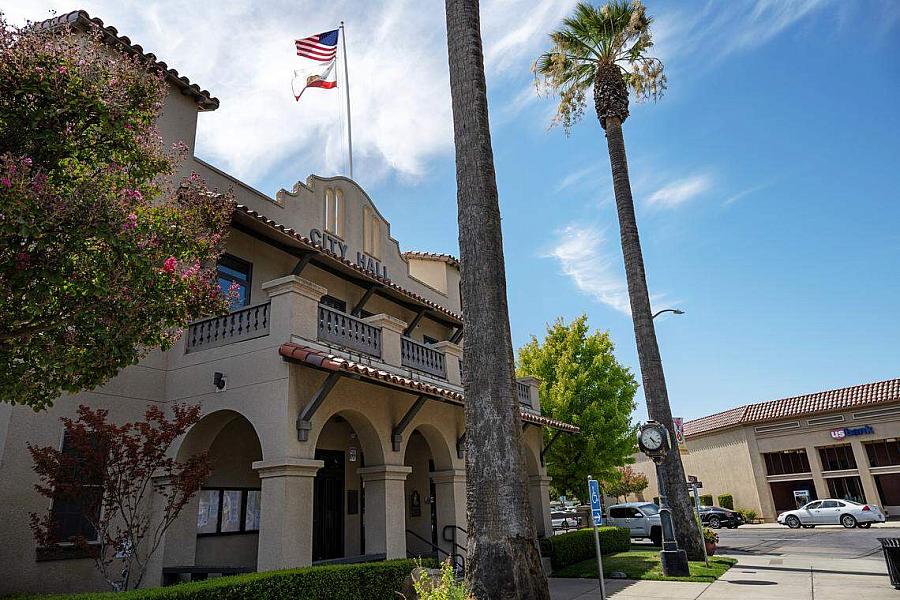 City Hall building — Patterson City Hall with palm trees and U.S. and California flags flying above.