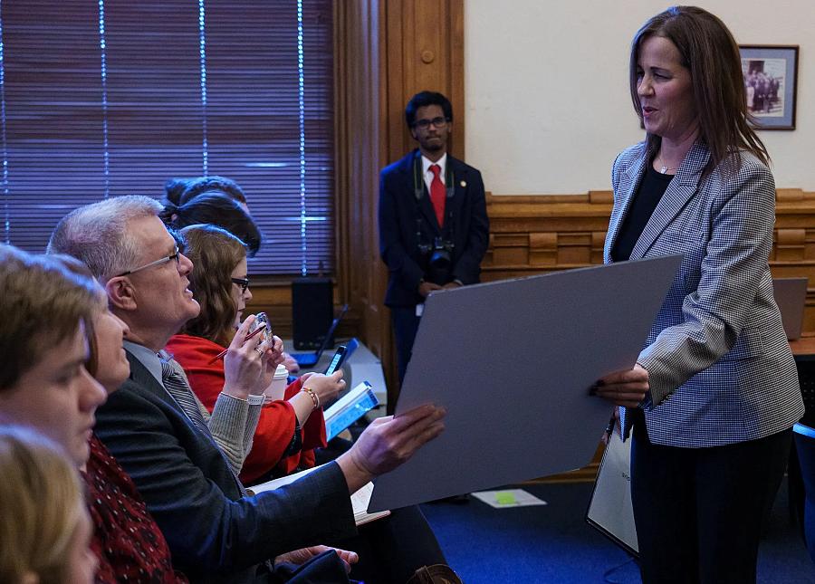 Julie West showing poster of athletic trainer in committee meeting.