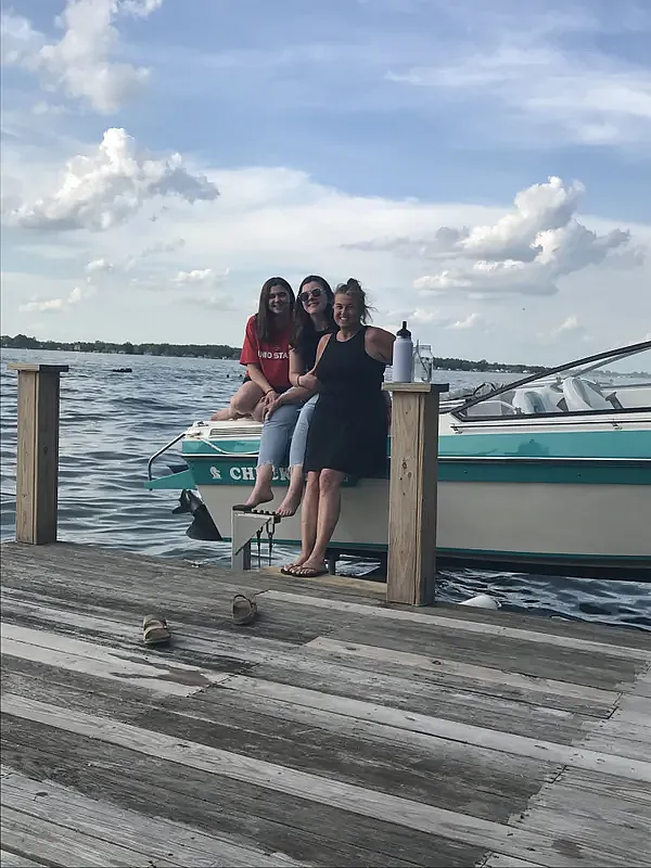 Three people at a pier sitting against a boat