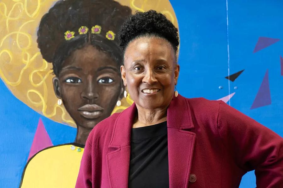 Woman in a burgundy blazer smiling in front of a mural of a girl.