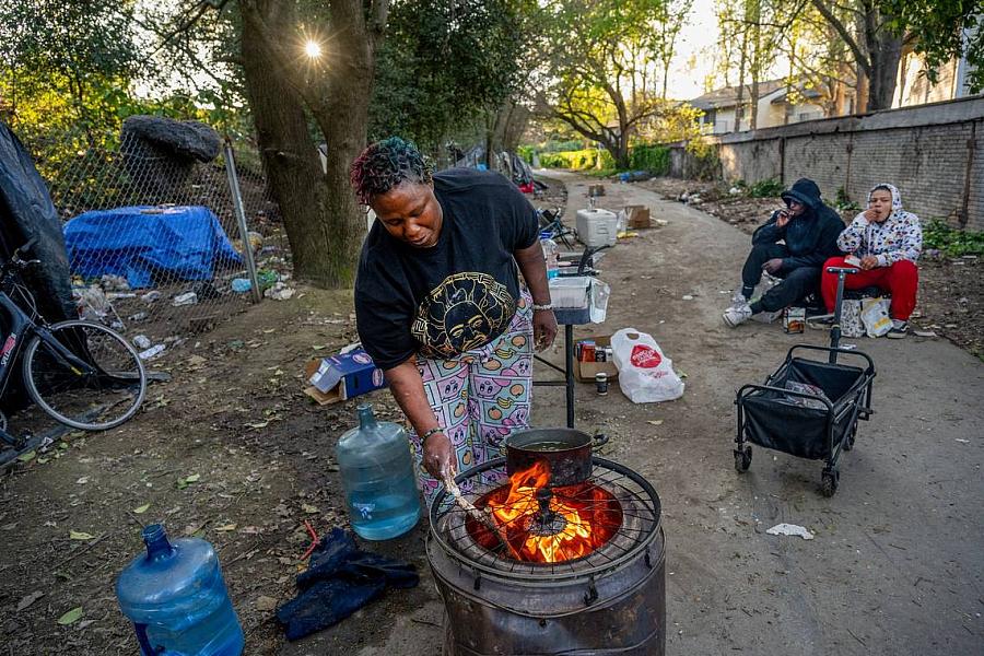 Woman tends to a cooking pot on an open fire in a makeshift outdoor kitchen.