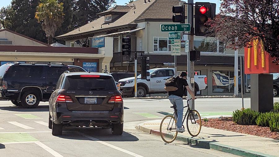 Cyclist rides onto curb at red light next to McDonald’s on Ocean Street, near waiting cars in bike lane.