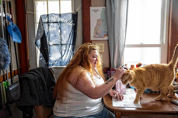 Woman pets orange cat while sitting at table.