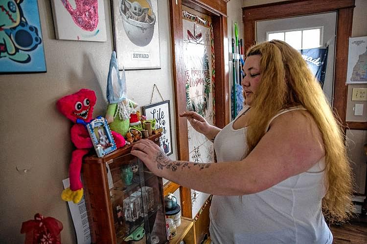 Woman stands near a display shelf with toys and photos.