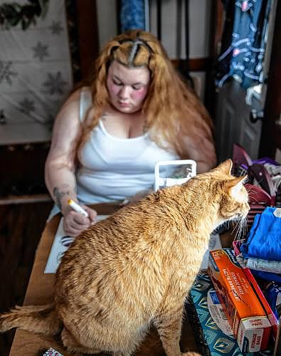 Orange cat sits on table near woman drawing.