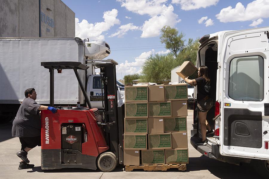 Workers load boxes labeled “farm fresh locally grown” onto a delivery van.