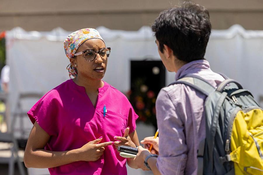 Two people talking to each other, one wearing pink top and other purple with a bag-pack