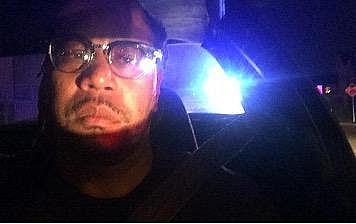 An image of a person sitting in car with the police car behind them.