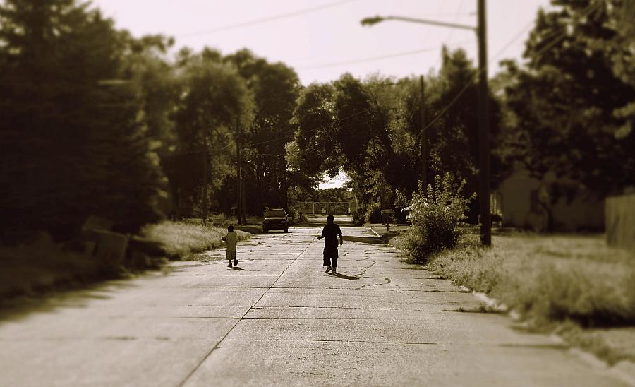 two children walking in the street between trees