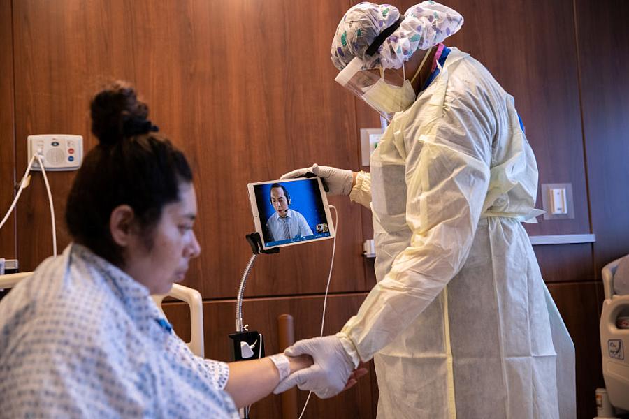 A hospital worker speaks through a remote Spanish translator while preparing a COVID-19 patient take her first steps after being