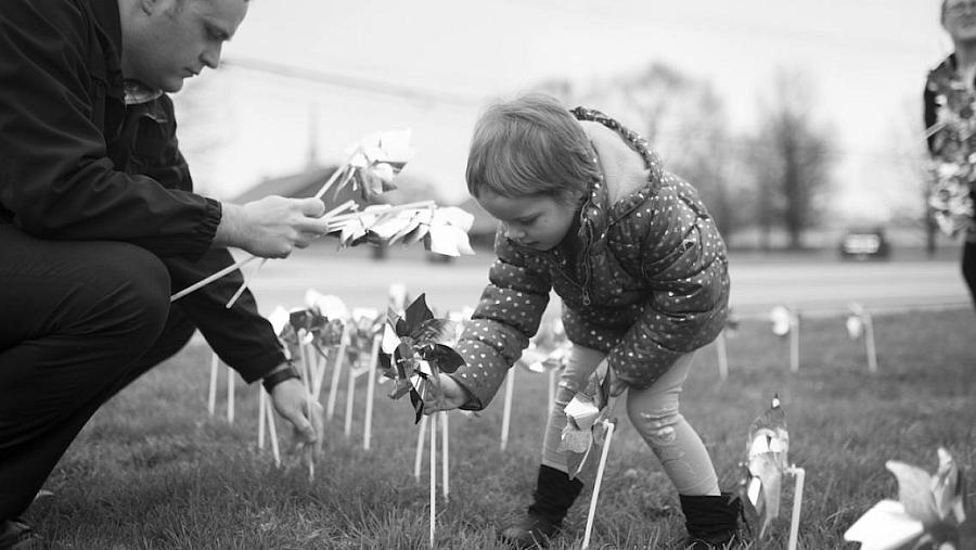 A young girl places pinwheels in the ground with a detective at the Bentonville Police Station at a rally to raise awareness of 