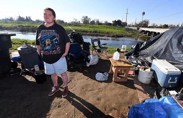 Becky Walthan, 45, stands outside of her tent along the east bank of the Stockton Diverting Canal. 