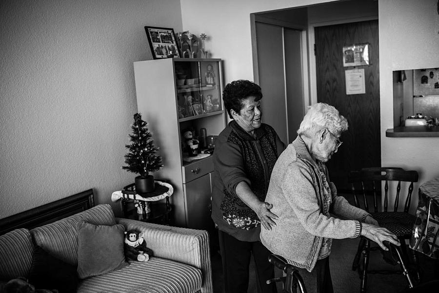 Maria Martínez helps her client, Agripina Castellanos, as she walks inside her Angelus Plaza apartment. (Photo by Bear Guerra)