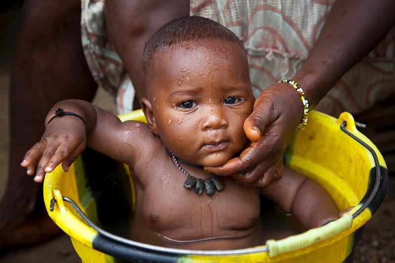 A baby being bathed in a basin. Mother's survival is key to child's wellbeing