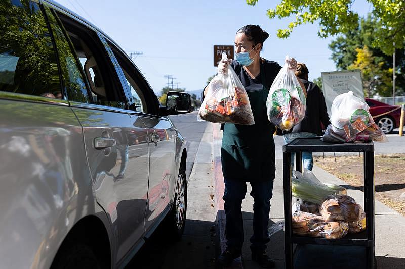 Norma Lazcano lifts bags of food into a client's car at a food pick-up site at the Los Robles Ronald McNair Academy in East Palo Alto on May 19, 2021. Photo by Magali Gauthier.