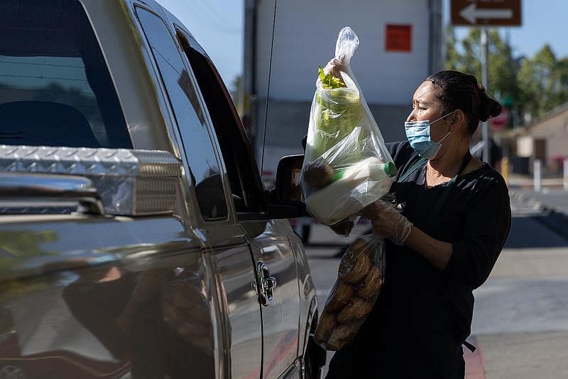 Norma Lazcano places bags of food in a client's car at a food pick-up site at the Los Robles Ronald McNair Academy in East Palo Alto on May 19, 2021. Photo by Magali Gauthier.